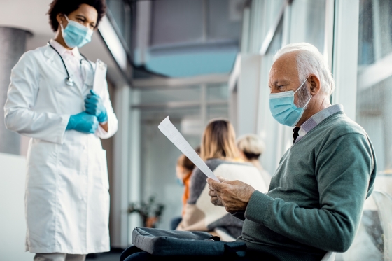 A health professional stands in front of a patient holding a sheet of paper